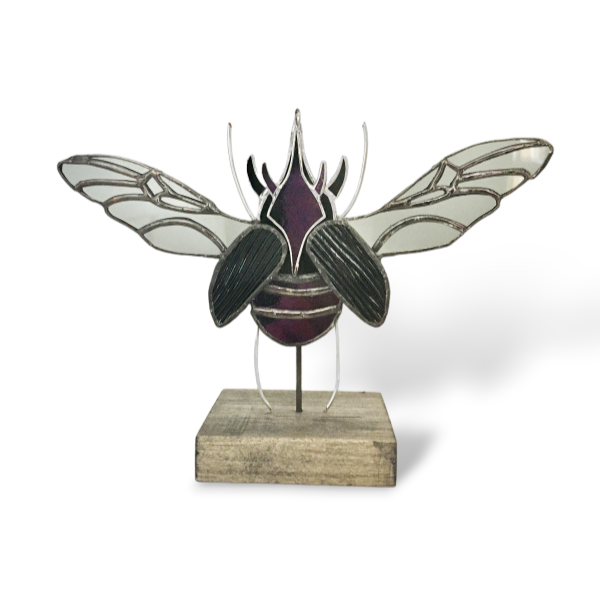 Sculpture en vitrail d'un coléoptère noir, gris et iridescent sur socle en bois.